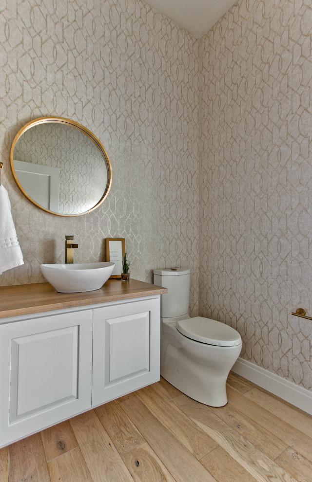 Foto på ett funkis brun toalett, med luckor med upphöjd panel, vita skåp, en toalettstol med separat cisternkåpa, beige väggar, ljust trägolv, ett fristående handfat, träbänkskiva och brunt golv