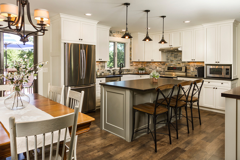 This is an example of a mid-sized transitional l-shaped eat-in kitchen in Minneapolis with a farmhouse sink, shaker cabinets, white cabinets, granite benchtops, blue splashback, stone tile splashback, stainless steel appliances, medium hardwood floors, with island, brown floor and black benchtop.