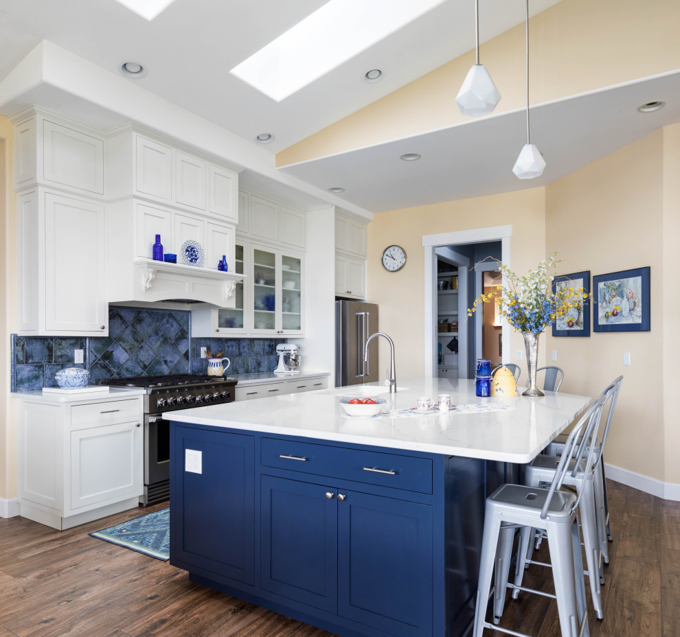This is an example of a large transitional galley open plan kitchen in Seattle with an undermount sink, shaker cabinets, quartz benchtops, blue splashback, ceramic splashback, stainless steel appliances, porcelain floors, with island, brown floor, white benchtop and white cabinets.