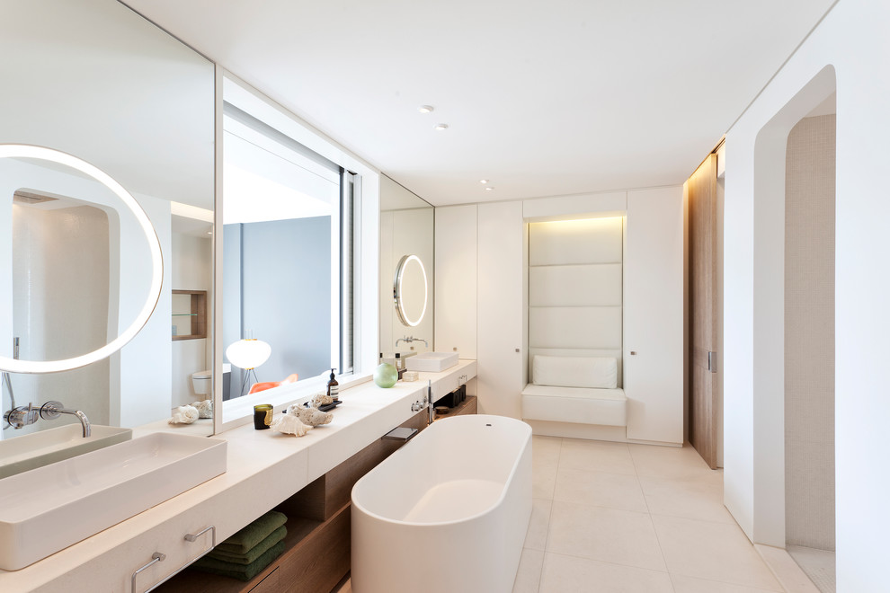 Mid-sized contemporary master bathroom in Berlin with flat-panel cabinets, white cabinets, a freestanding tub, a curbless shower, a wall-mount toilet, beige tile, stone slab, white walls, limestone floors, a vessel sink and limestone benchtops.