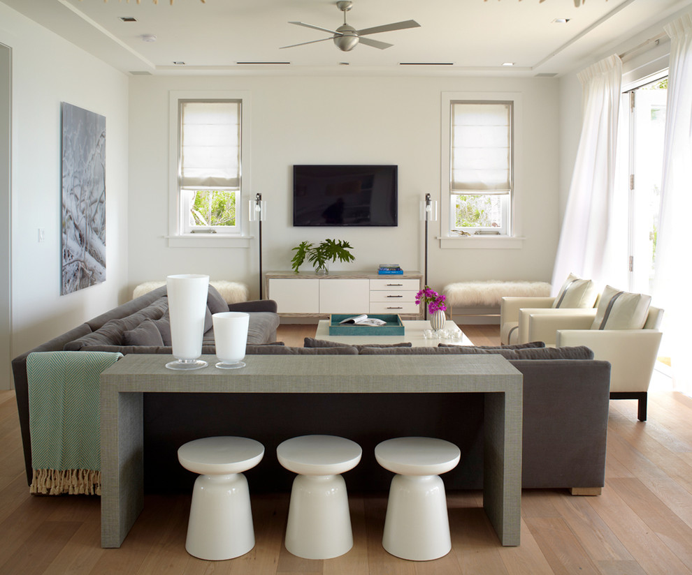 This is an example of a beach style family room in New York with white walls, medium hardwood floors, no fireplace, a wall-mounted tv and brown floor.