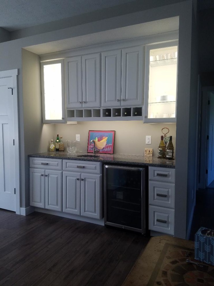 Mid-sized country single-wall wet bar in Other with an undermount sink, raised-panel cabinets, white cabinets, granite benchtops, laminate floors and brown floor.