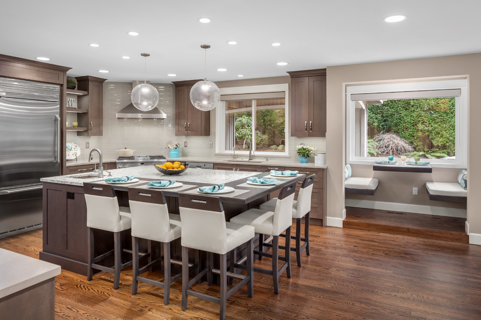 Eat-in kitchen - large transitional u-shaped medium tone wood floor and brown floor eat-in kitchen idea in Seattle with a single-bowl sink, shaker cabinets, dark wood cabinets, quartzite countertops, gray backsplash, glass tile backsplash, stainless steel appliances, an island and white countertops