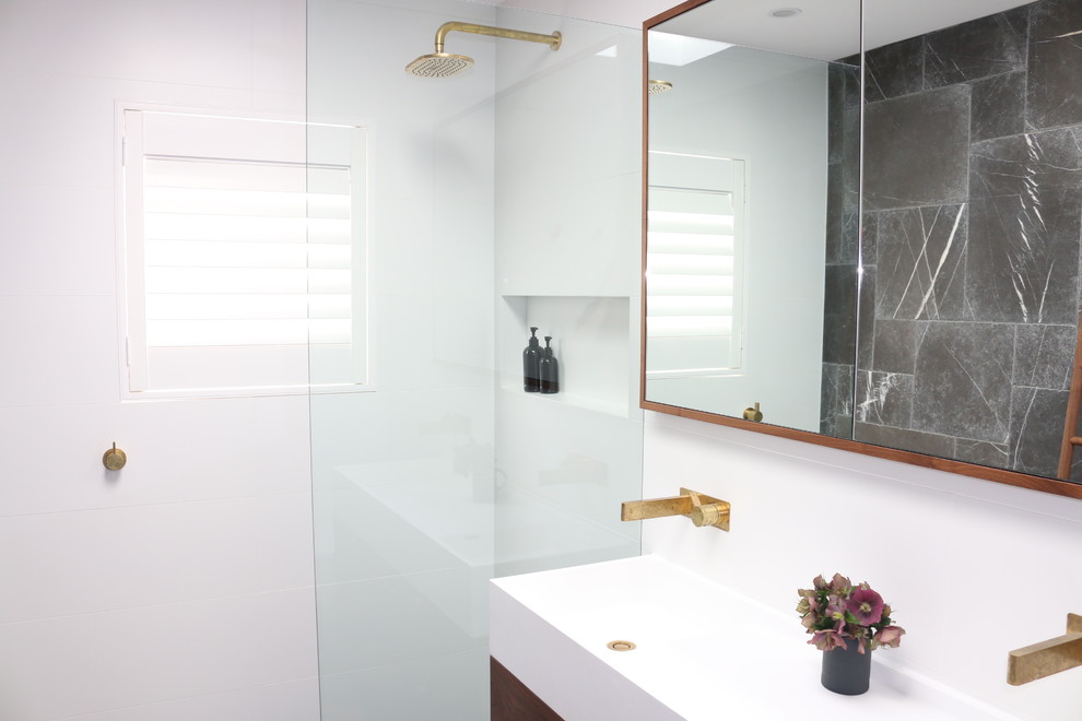 This is an example of a mid-sized contemporary 3/4 bathroom in Sydney with furniture-like cabinets, brown cabinets, an open shower, white tile, porcelain tile, limestone floors, an integrated sink, solid surface benchtops, grey floor, an open shower and white benchtops.