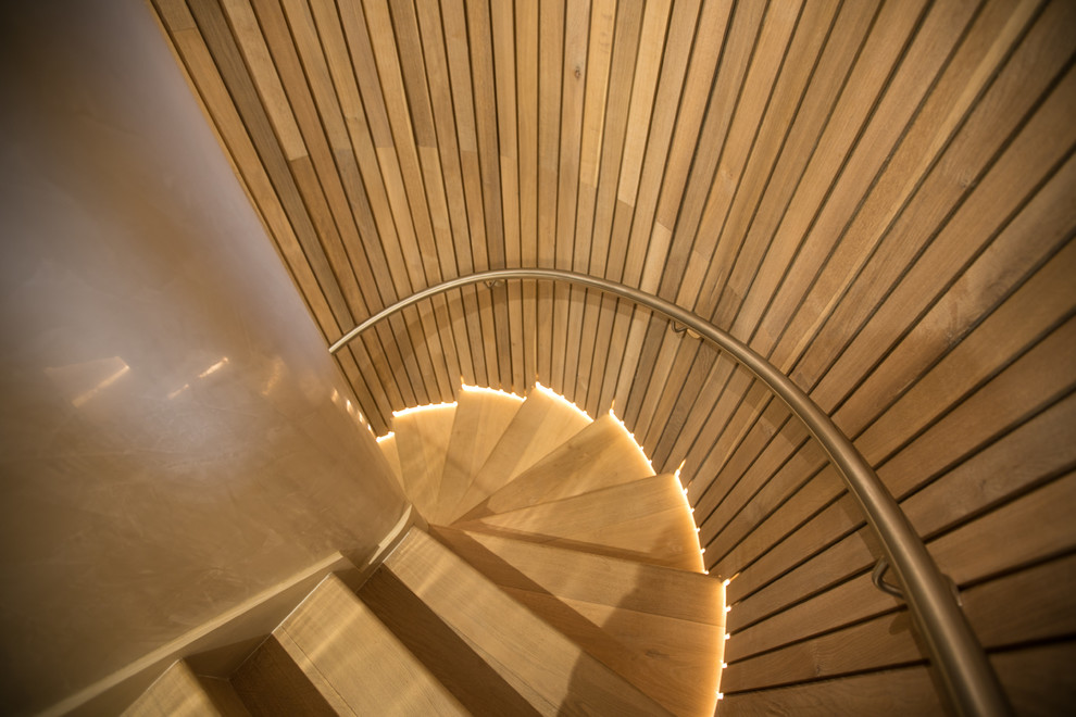 Mid-sized contemporary wood spiral staircase in London with wood risers and metal railing.
