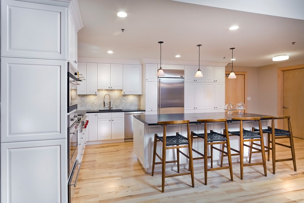 This is an example of a transitional kitchen in Minneapolis with an undermount sink, raised-panel cabinets, white cabinets, stainless steel appliances, light hardwood floors and with island.