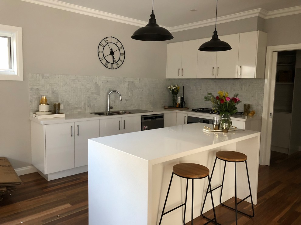 This is an example of a mid-sized contemporary l-shaped eat-in kitchen in Other with a drop-in sink, granite benchtops, grey splashback, marble splashback, medium hardwood floors, with island, brown floor and white benchtop.