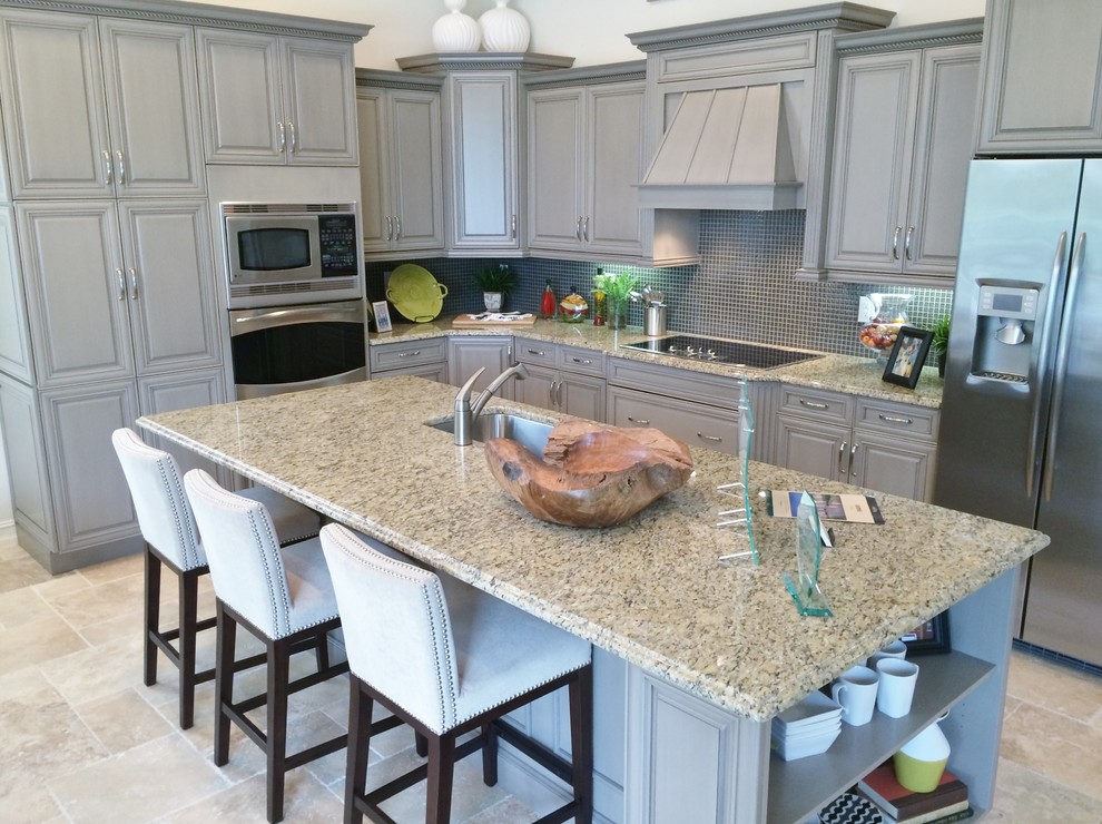 Large transitional l-shaped travertine floor eat-in kitchen photo in Tampa with an undermount sink, raised-panel cabinets, gray cabinets, granite countertops, black backsplash, glass tile backsplash, stainless steel appliances and an island