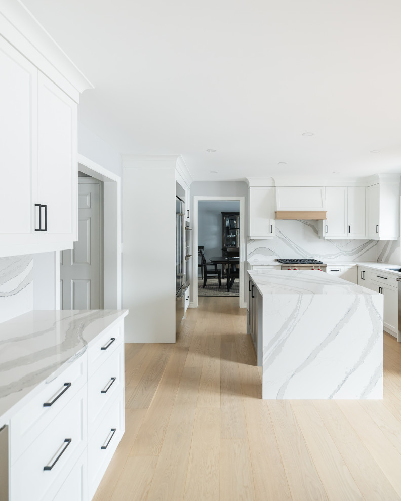 Example of a mid-sized transitional u-shaped light wood floor eat-in kitchen design in Toronto with an undermount sink, shaker cabinets, white cabinets, quartz countertops, white backsplash, quartz backsplash, stainless steel appliances, an island and white countertops