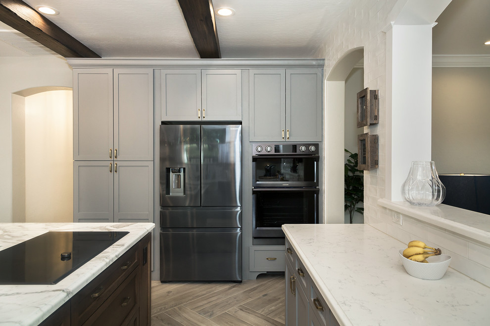 Example of a large transitional l-shaped porcelain tile and brown floor eat-in kitchen design in Phoenix with a farmhouse sink, shaker cabinets, gray cabinets, quartz countertops, white backsplash, glass sheet backsplash, stainless steel appliances, an island and white countertops