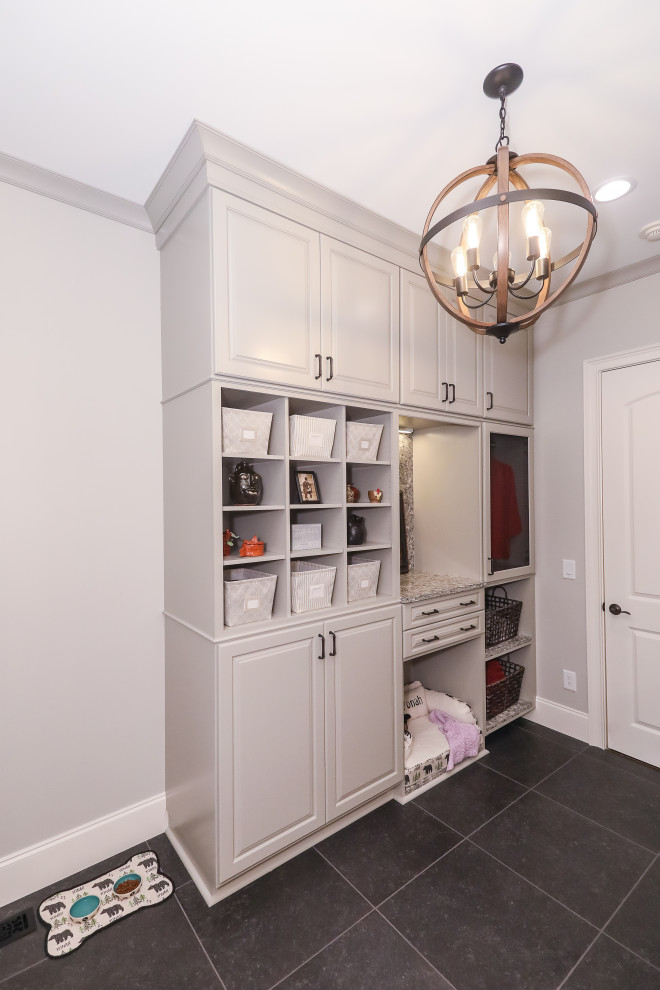 This is an example of a large transitional galley dedicated laundry room in Atlanta with a farmhouse sink, raised-panel cabinets, grey cabinets, quartz benchtops, multi-coloured splashback, engineered quartz splashback, grey walls, porcelain floors, a side-by-side washer and dryer, black floor and multi-coloured benchtop.