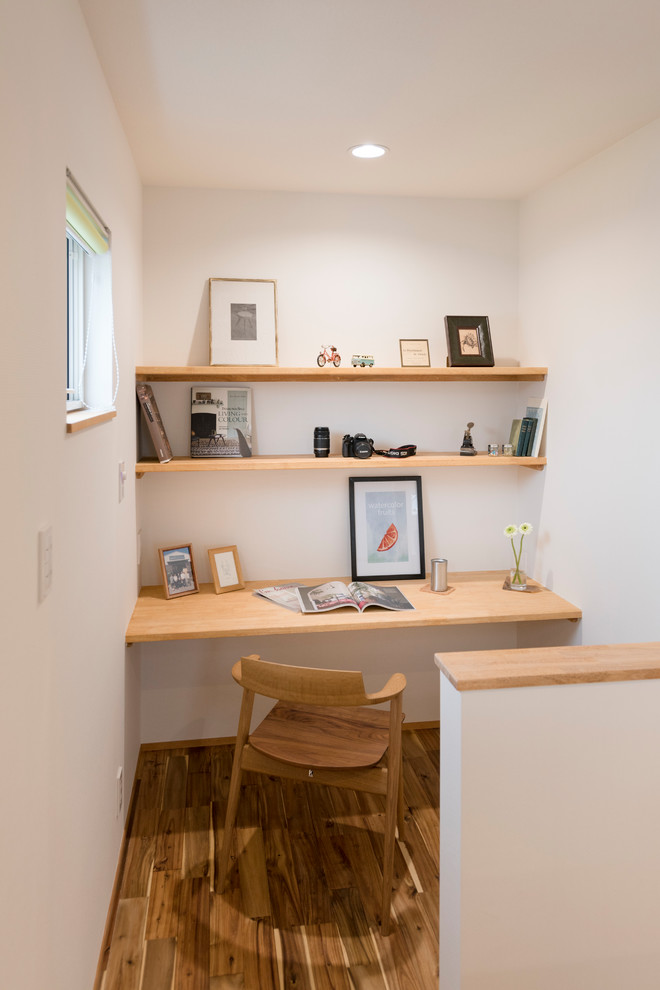 Asian home office in Nagoya with white walls, painted wood floors, a built-in desk and brown floor.