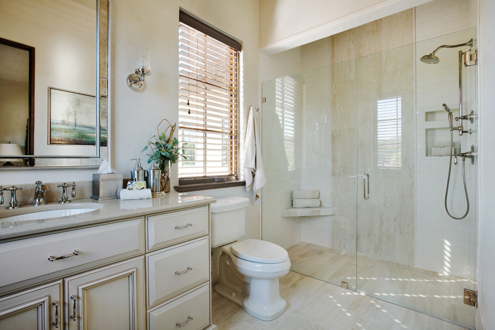 This is an example of a mediterranean 3/4 bathroom in Other with raised-panel cabinets, a curbless shower, travertine floors, beige cabinets, a two-piece toilet, beige tile, subway tile, beige walls, an undermount sink, engineered quartz benchtops, beige floor and a hinged shower door.