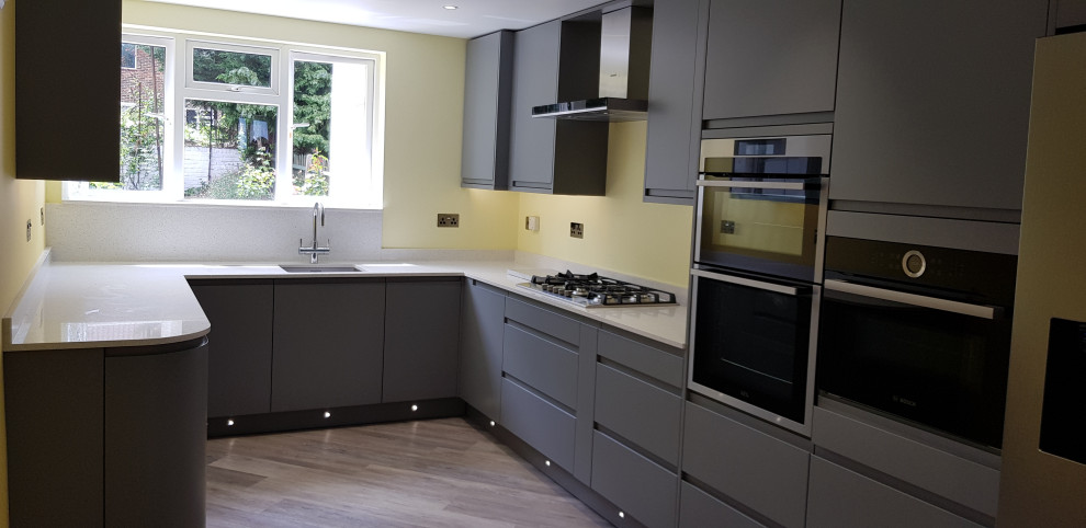 Inspiration for a mid-sized contemporary u-shaped eat-in kitchen in London with an undermount sink, flat-panel cabinets, grey cabinets, quartzite benchtops, yellow splashback, glass sheet splashback, black appliances, vinyl floors, no island, grey floor and white benchtop.