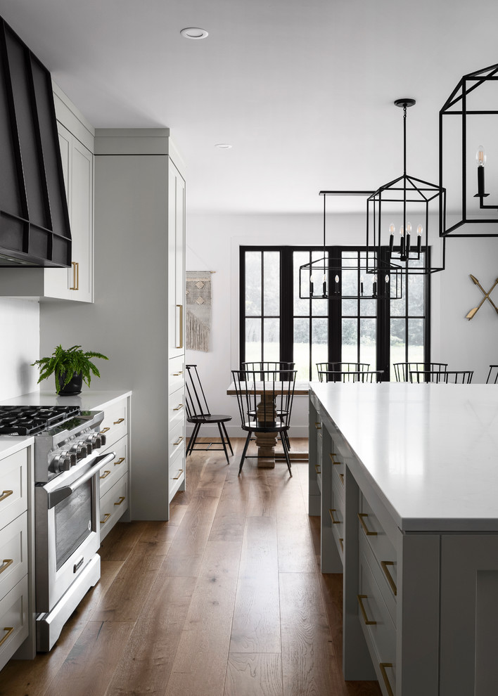 Design ideas for a large country single-wall eat-in kitchen in Toronto with a farmhouse sink, shaker cabinets, grey cabinets, quartz benchtops, white splashback, subway tile splashback, stainless steel appliances, light hardwood floors, with island, brown floor and grey benchtop.