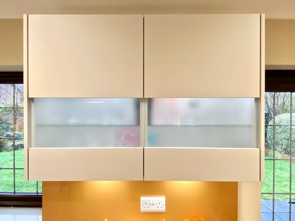Design ideas for a mid-sized contemporary l-shaped open plan kitchen in Sussex with an undermount sink, flat-panel cabinets, white cabinets, quartzite benchtops, yellow splashback, glass sheet splashback, panelled appliances, vinyl floors, with island, brown floor and grey benchtop.