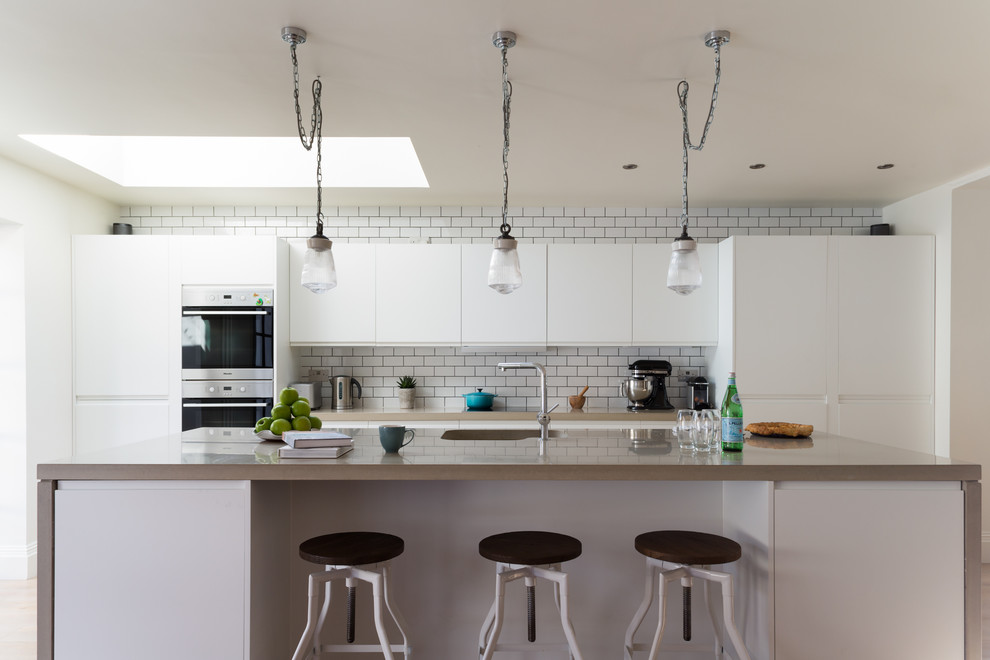 Design ideas for a transitional kitchen in London with a single-bowl sink, flat-panel cabinets, white cabinets, white splashback, subway tile splashback, with island and concrete benchtops.