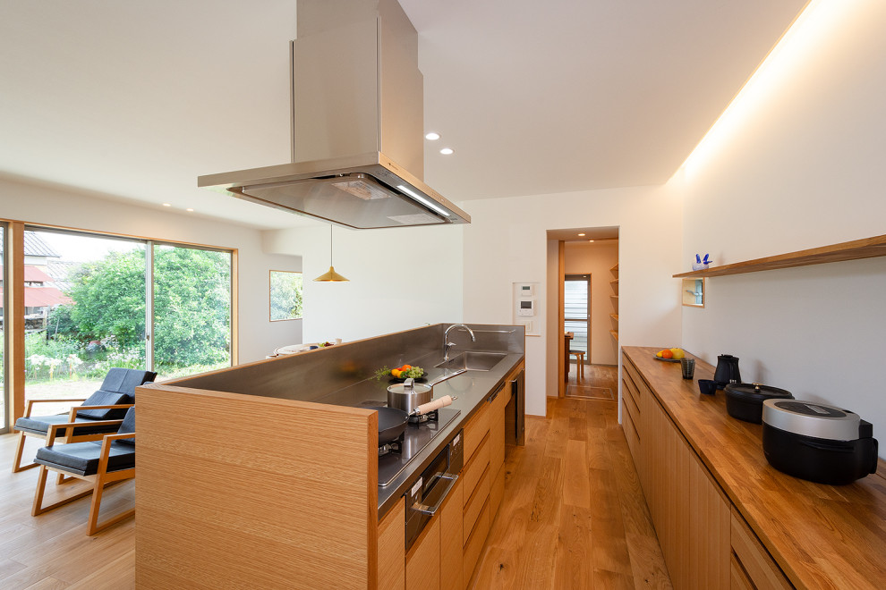 Foto på ett stort minimalistiskt brun linjärt kök med öppen planlösning, med en integrerad diskho, släta luckor, skåp i mellenmörkt trä, bänkskiva i rostfritt stål, stänkskydd med metallisk yta, svarta vitvaror, mellanmörkt trägolv, en köksö och brunt golv