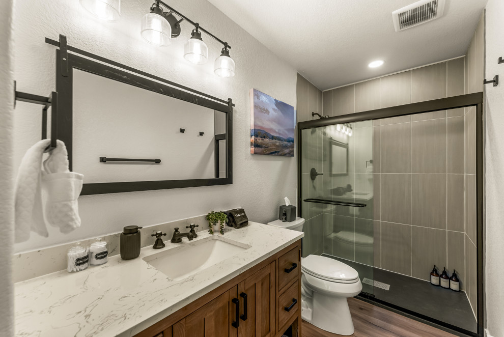 Example of a small mountain style master gray tile and ceramic tile laminate floor, brown floor and single-sink sliding shower door design with black cabinets, a two-piece toilet, white walls, a drop-in sink, granite countertops, white countertops, a built-in vanity and shaker cabinets