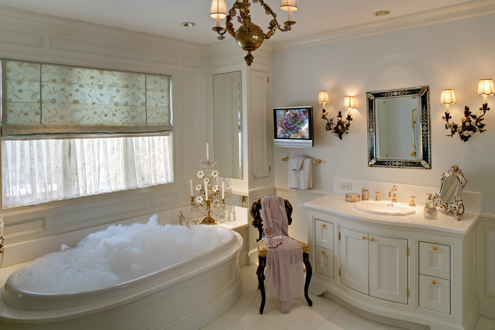 This is an example of a traditional bathroom in New York with shaker cabinets, white cabinets, a drop-in tub, white tile, white walls, a drop-in sink and white floor.