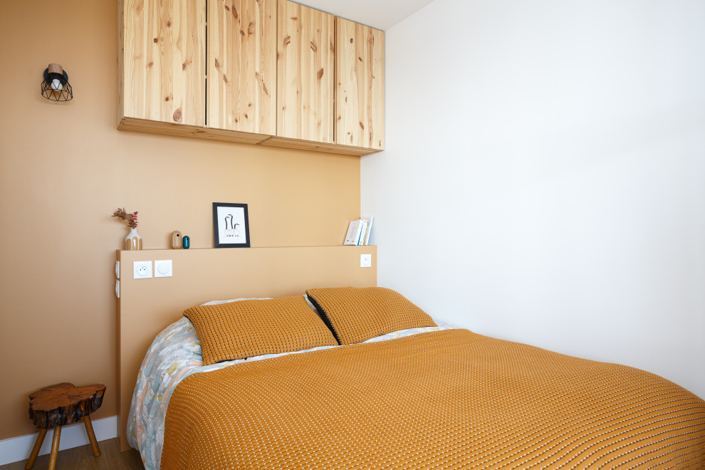 Cette image montre une petite chambre parentale nordique avec un mur orange et un sol en bois brun.