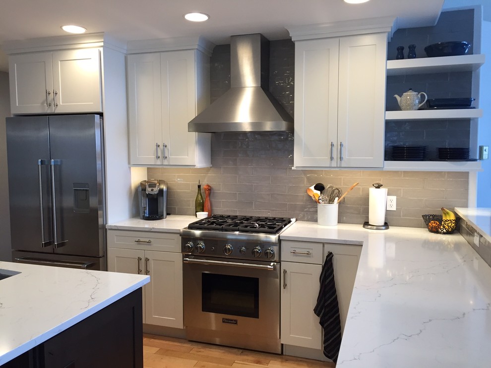 Transitional l-shaped light wood floor open concept kitchen photo with an undermount sink, recessed-panel cabinets, white cabinets, quartz countertops, gray backsplash, ceramic backsplash, stainless steel appliances and an island