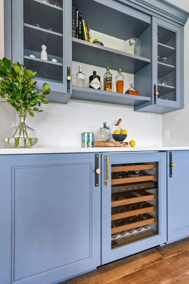 This is an example of a mid-sized beach style l-shaped open plan kitchen in Other with a farmhouse sink, shaker cabinets, blue cabinets, quartz benchtops, white splashback, porcelain splashback, black appliances, porcelain floors, with island, brown floor, white benchtop and timber.