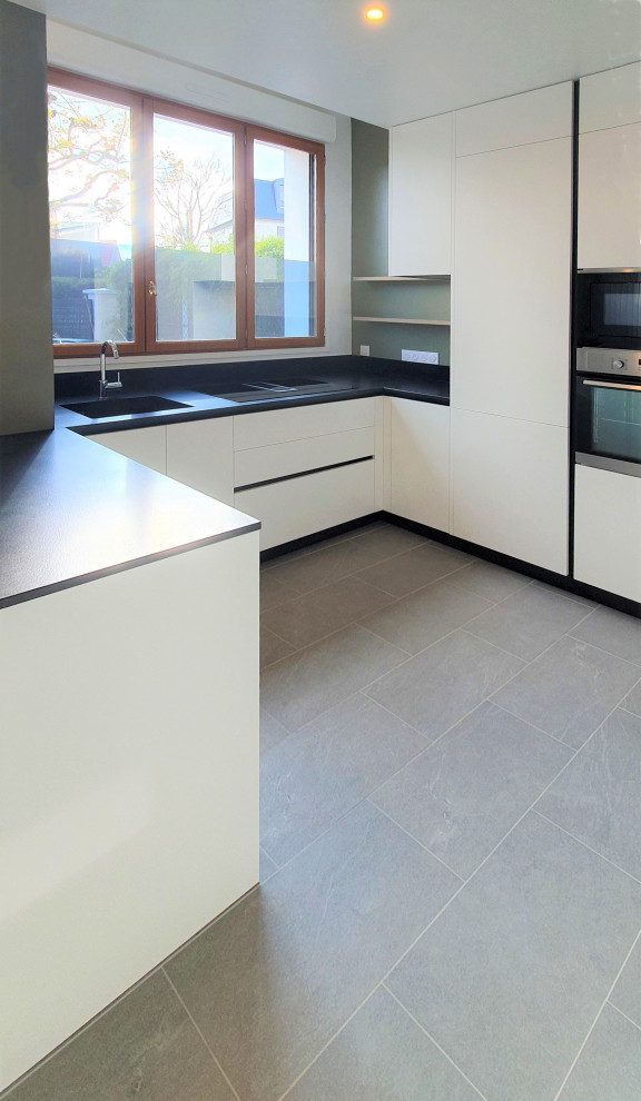 Expansive modern single-wall open plan kitchen in Other with an integrated sink, flat-panel cabinets, white cabinets, granite benchtops, black splashback, granite splashback, panelled appliances, cement tiles, with island, grey floor and black benchtop.