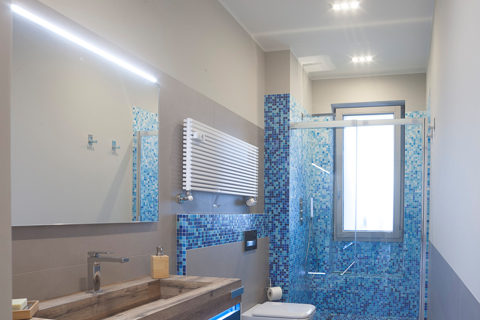 Inredning av ett modernt mellanstort flerfärgad flerfärgat badrum med dusch, med släta luckor, blå skåp, en kantlös dusch, en vägghängd toalettstol, flerfärgad kakel, porslinskakel, grå väggar, klinkergolv i porslin, ett integrerad handfat, träbänkskiva, grått golv och dusch med skjutdörr