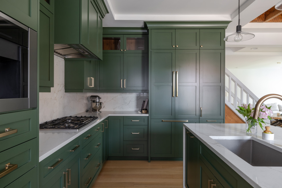 Inspiration for a large transitional l-shaped eat-in kitchen in Detroit with an undermount sink, shaker cabinets, green cabinets, quartz benchtops, white splashback, engineered quartz splashback, stainless steel appliances, light hardwood floors, with island, brown floor, white benchtop and recessed.