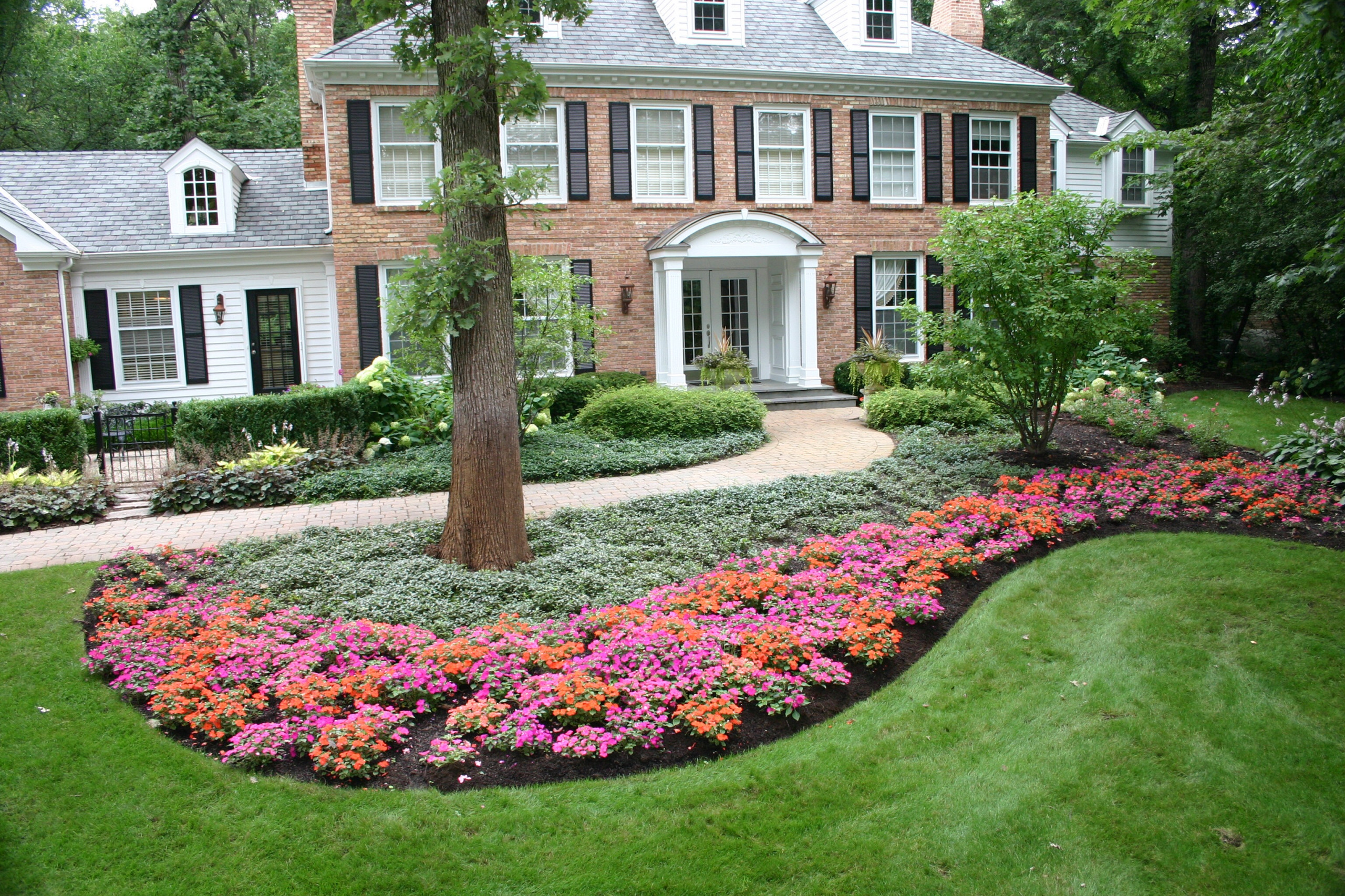 Here we used pots at the front door, pachysandra as a ground cover and a large bed of orange and hot pink new impatient to capture this welcome to this brick home. Peter Atkins and Associates