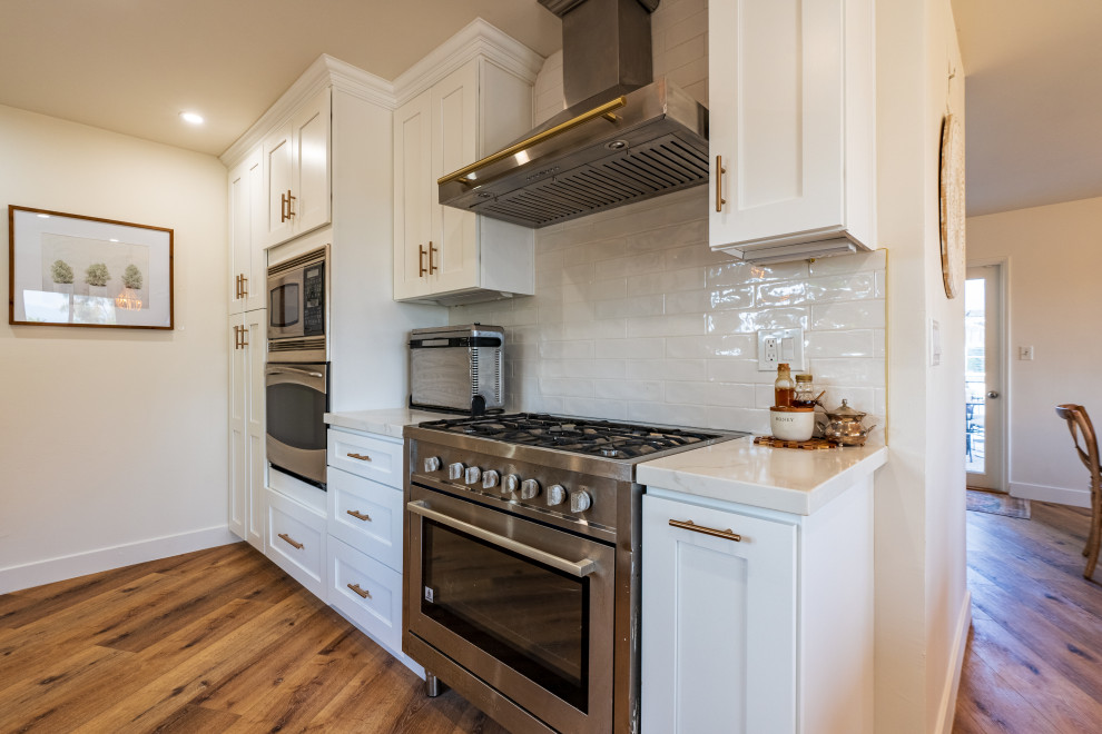 Idéer för att renovera ett mellanstort eklektiskt vit vitt kök, med en rustik diskho, luckor med profilerade fronter, vita skåp, marmorbänkskiva, grått stänkskydd, stänkskydd i marmor, rostfria vitvaror, plywoodgolv, en köksö och brunt golv