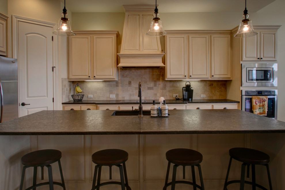 Example of a mountain style kitchen pantry design in Austin with an undermount sink, raised-panel cabinets, white cabinets, granite countertops, beige backsplash, travertine backsplash, stainless steel appliances, an island and black countertops