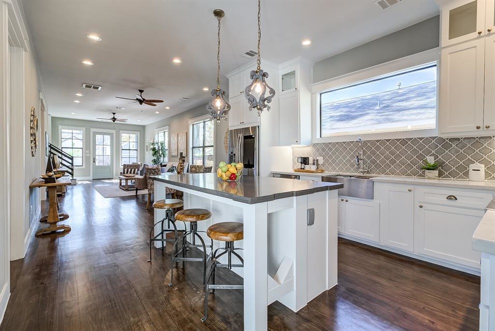 Photo of a mid-sized arts and crafts l-shaped open plan kitchen in Houston with a farmhouse sink, shaker cabinets, white cabinets, concrete benchtops, grey splashback, ceramic splashback, stainless steel appliances, dark hardwood floors, with island, brown floor and grey benchtop.