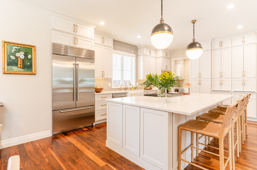 Inspiration for a large transitional l-shaped dark wood floor and brown floor open concept kitchen remodel in Denver with a farmhouse sink, shaker cabinets, beige cabinets, quartz countertops, beige backsplash, ceramic backsplash, stainless steel appliances, an island and white countertops