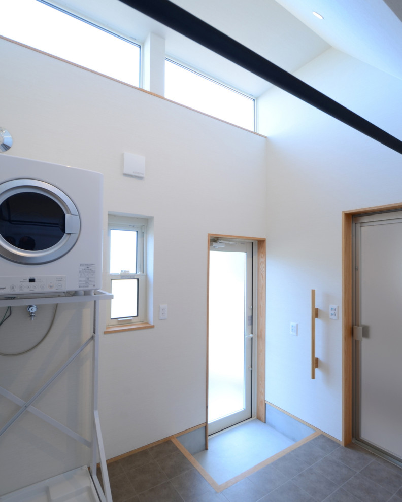 Photo of a mid-sized dedicated laundry room in Other with white walls, wallpaper, wallpaper, terra-cotta floors, a stacked washer and dryer and grey floor.