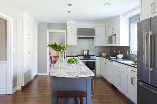 Bright galley-style kitchen with white shaker kitchen cabinet doors, gray island with stone countertop, stainless steel appliances, and subway tile backsplash.