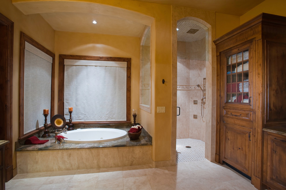 Example of a large mountain style master beige tile and stone tile limestone floor and beige floor drop-in bathtub design in Denver with medium tone wood cabinets, granite countertops, beige walls and furniture-like cabinets