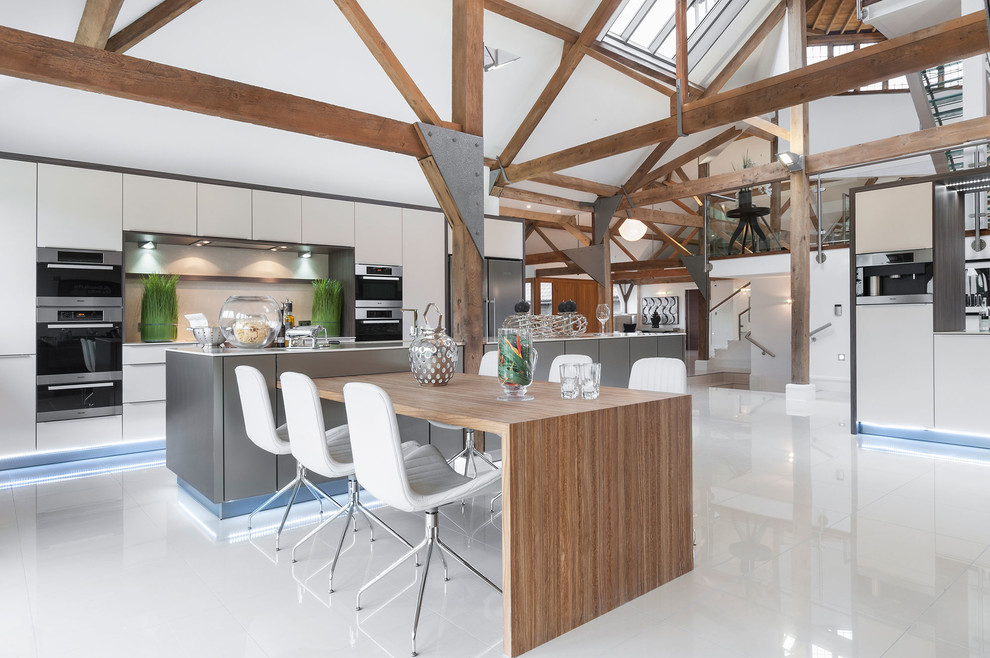 Design ideas for an expansive industrial open plan kitchen in Hampshire with flat-panel cabinets, white cabinets, solid surface benchtops, white splashback, multiple islands, white floor and stainless steel appliances.