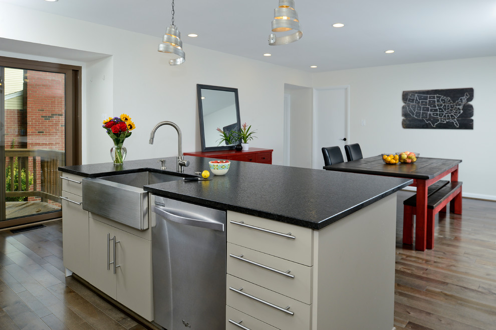 Mid-sized modern single-wall eat-in kitchen in DC Metro with a farmhouse sink, flat-panel cabinets, granite benchtops, brown splashback, mosaic tile splashback, stainless steel appliances, dark hardwood floors, with island and beige cabinets.