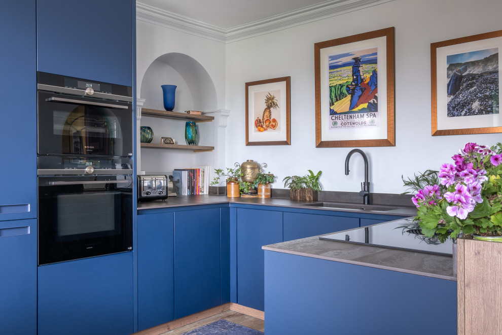 Diseño de cocinas en U contemporáneo pequeño cerrado con fregadero encastrado, armarios con paneles lisos, puertas de armario azules, encimera de acrílico, electrodomésticos negros y encimeras grises