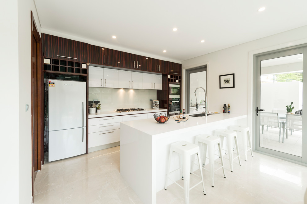 This is an example of a large modern galley kitchen pantry in Canberra - Queanbeyan with a drop-in sink, recessed-panel cabinets, granite benchtops, white splashback, glass sheet splashback, stainless steel appliances, ceramic floors, with island and white benchtop.