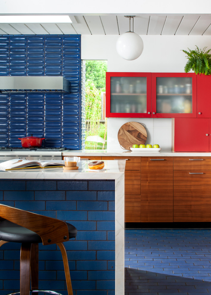 Photo of a midcentury open plan kitchen with flat-panel cabinets, medium wood cabinets, quartzite benchtops, white splashback, glass tile splashback, stainless steel appliances, brick floors, with island, blue floor, white benchtop and timber.
