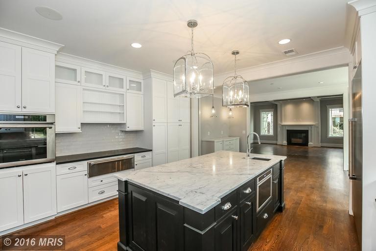 Photo of a large transitional u-shaped separate kitchen in DC Metro with a farmhouse sink, shaker cabinets, white cabinets, granite benchtops, grey splashback, stainless steel appliances, medium hardwood floors and with island.