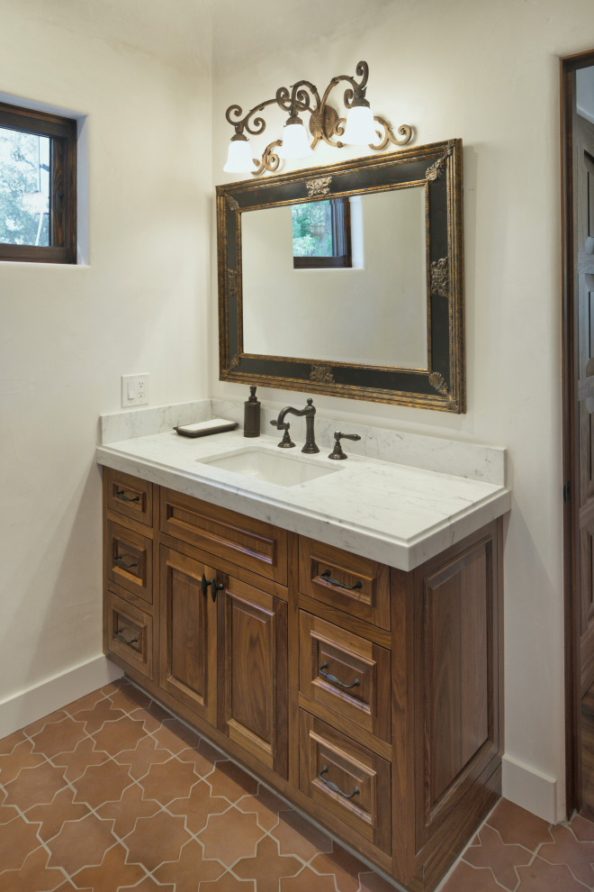 Bild på ett mellanstort medelhavsstil vit vitt badrum, med luckor med upphöjd panel, skåp i mellenmörkt trä, vita väggar, klinkergolv i porslin, ett undermonterad handfat, marmorbänkskiva och rött golv