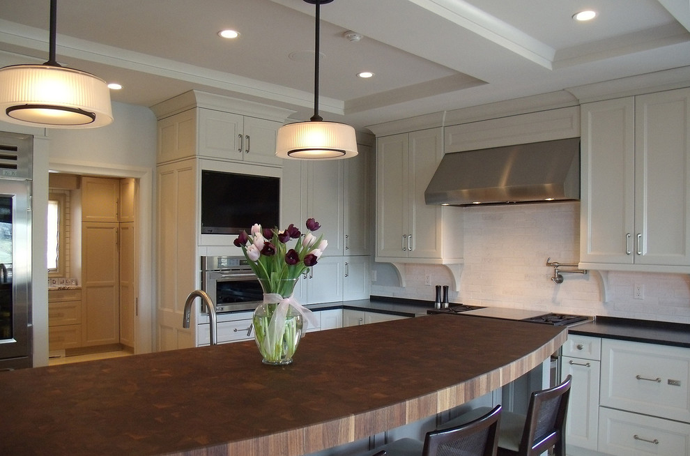 Enclosed kitchen - mid-sized transitional l-shaped porcelain tile and beige floor enclosed kitchen idea with recessed-panel cabinets, white cabinets, wood countertops, white backsplash, subway tile backsplash, stainless steel appliances, an island and an undermount sink