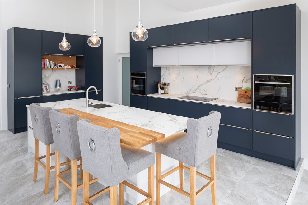 This is an example of a mid-sized contemporary galley kitchen in Other with an undermount sink, flat-panel cabinets, blue cabinets, grey splashback, black appliances, with island, grey floor and grey benchtop.
