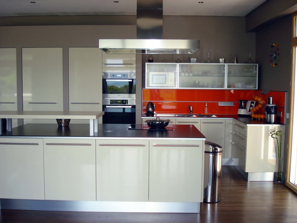 Design ideas for a large modern galley eat-in kitchen in Le Havre with a double-bowl sink, flat-panel cabinets, beige cabinets, laminate benchtops, orange splashback, glass sheet splashback, stainless steel appliances, plywood floors, with island and brown floor.