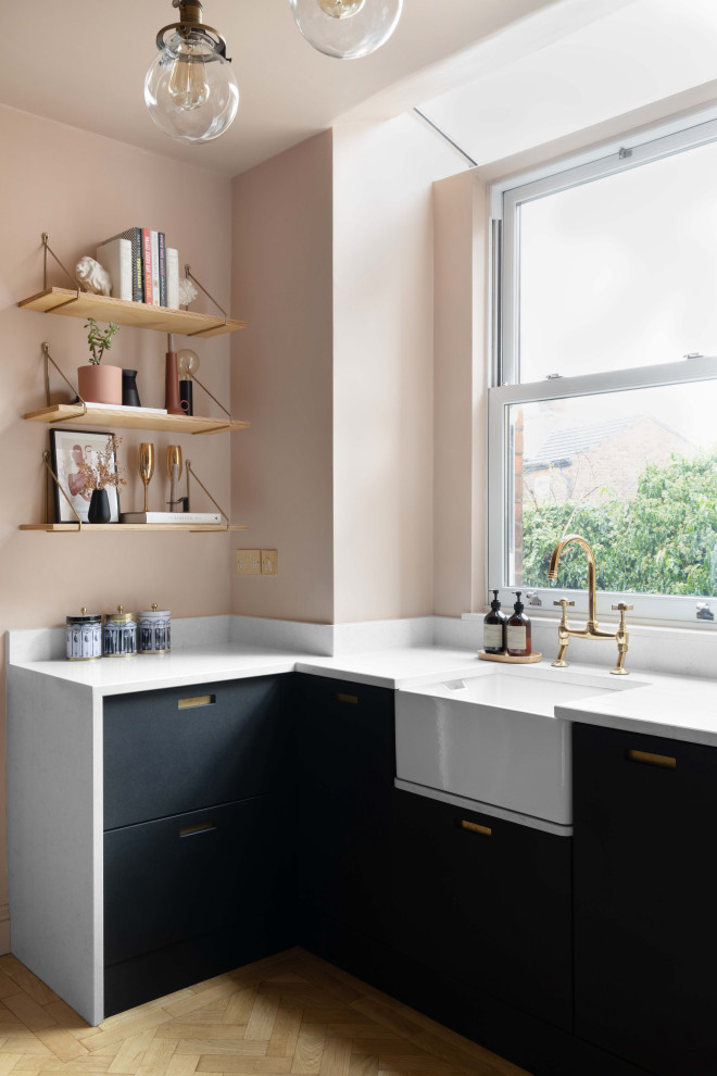 Foto di una cucina a L minimalista di medie dimensioni con lavello stile country, ante lisce, ante nere, top in quarzite, parquet chiaro, nessuna isola e top bianco