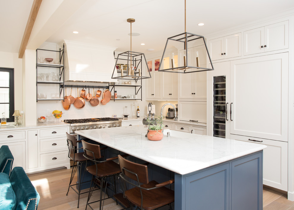Design ideas for a transitional kitchen in Orange County with a farmhouse sink, shaker cabinets, blue cabinets, white splashback, subway tile splashback, panelled appliances, light hardwood floors and with island.
